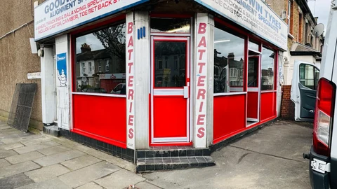 Red-framed corner shopfront with glazed entrance and lower infill panels.